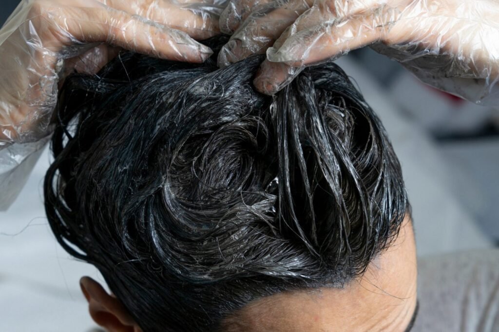 Woman wearing plastic gloves spplying dark hair dye to her hair